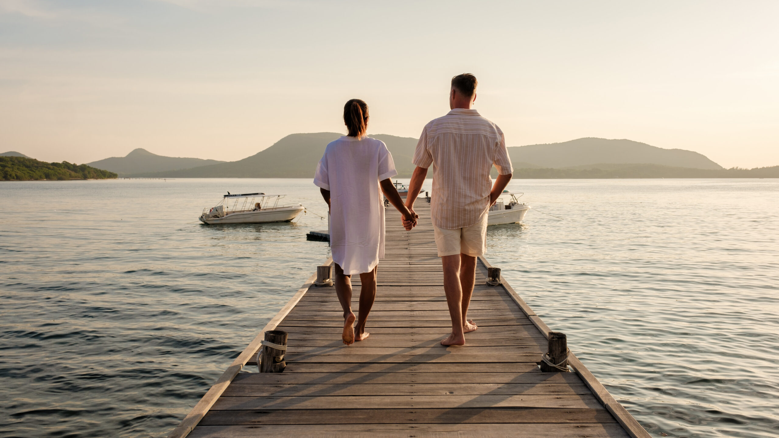 A couple of European men and an Asian woman on vacation in Thailand, couple walking at a wooden pier in the ocean during sunset in Samaesan Thailand