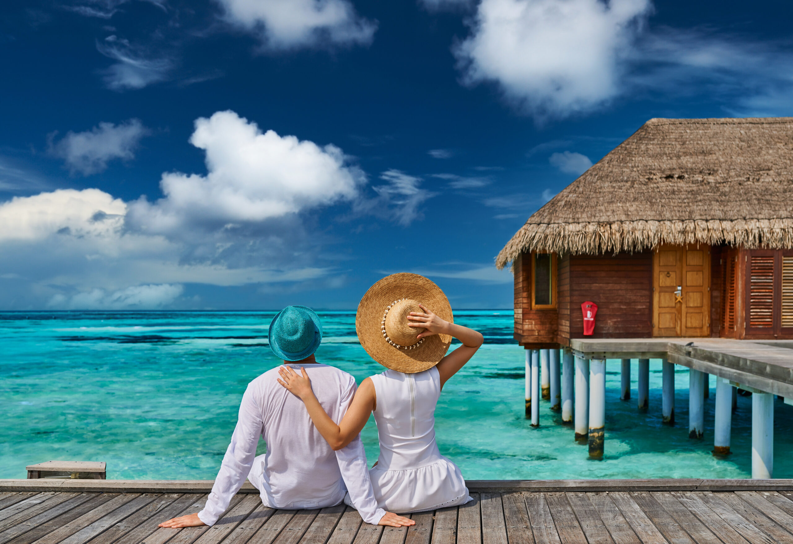 Couple in white on a tropical beach jetty near water villa at Maldives